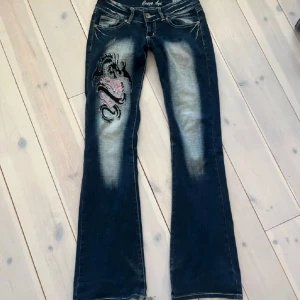 Crazy Age y2k  - Snygga blå jeans från Crazy Age med ett coolt drakbroderi i svart och rosa på benet. ❤️Ingen defekt på användning förutom längst ner vid foten på baksidan-se sista bild.💋❤️midjan-36 innerbenet-84!!