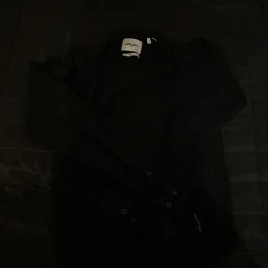 Svart jacka från Jack & Jones - Säljer en stilren svart jacka från Jack & Jones Core. Jackan har en klassisk design med knappar och dragkedja, perfekt för en cool och avslappnad look. Den är i en bekväm passform och passar bra till olika tillfällen.