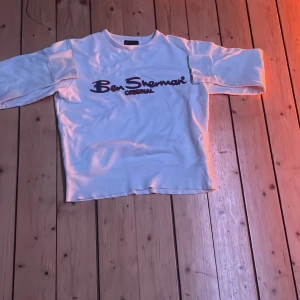 Vit tröja från Ben Sherman - Säljer en vit tröja från Ben Sherman med deras logga i mörk färg på framsidan. Tröjan har långa ärmar och en klassisk rund halsringning. Perfekt för en avslappnad stil. Går att pruta