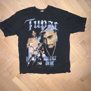 Tupac T-shirt från Junkyard - Cool svart T-shirt från Junkyard med stort Tupac-tryck på framsidan. Perfekt för dig som älskar hiphop och vill ha en statement-piece i garderoben. T-shirten har korta ärmar och en normal passform.
