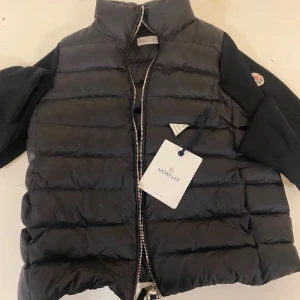 Svart pufferjacka från Moncler - Säljer en snygg svart pufferjacka/ cardigan från Moncler. Jackan har långa ärmar och en hög krage för extra värme. Aldrig använd då jag fick två jackor i julklapp. Går att skanna insidan storlek S. Medföljer taggen på bild samt Moncler påse.