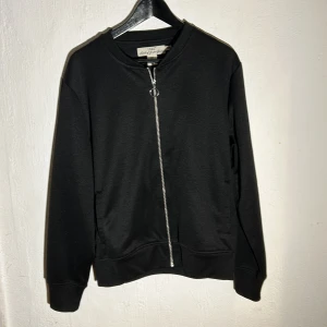 Svart tröja med dragkedja från H&M - Säljer en stilren svart tröja från H&M med dragkedja framtill. Tröjan har långa ärmar och en rund halsringning. Perfekt för en avslappnad look.