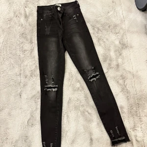 Svarta jeans med slitningar från Blue Rags - Snygga svarta jeans från Blue Rags med coola slitningar på låren och knäna. De har en tight passform och är perfekta för en avslappnad men stilren look. Jeansen har en knapp och dragkedja framtill samt klassiska fem fickor.