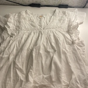 Vit blus från Gina Tricot - Säljer en söt vit blus från Gina Tricot i storlek 158/164. Blusen har fina volangdetaljer vid ärmarna och en v-ringad hals. Perfekt för sommardagar. Materialet känns lätt och luftigt, vilket gör den bekväm att bära hela dagen.