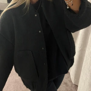  bomberjacka i boucle  - Säljer en snygg svart/marinblå boucle bomberjacka i mycket bra skick. Den har en klassisk design med knappar framtill och är perfekt för höst och vår. Jackan är långärmad och har en normal passform. Perfekt för att ge din outfit en cool touch!