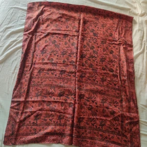 Sidensjal från Indien  - Säljer en elegant orange/röd/rostfärgad sidensjal med med ett vackert mönster. Perfekt för att ge en färgklick till din outfit. Den är mjuk och lätt, vilket gör den idealisk för både vår och sommar. Tillverkad i Indien.