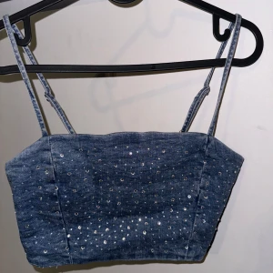 Blå jeanskorsett med paljetter - Snygg blå jeanskorsett med justerbara axelband och glittrande paljetter över hela ytan. Perfekt för en festlig kväll eller en utekväll med vänner. Den har en tight passform som framhäver figuren. Storlek M men känns som en S