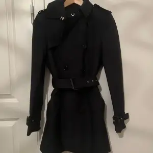 Snygg svart trenchcoat från Zara i mycket bra skick. Den har en klassisk design med knappar och ett bälte i midjan för en elegant look. Perfekt för höst och vår, med långa ärmar och en stilren passform. Nypris 1000