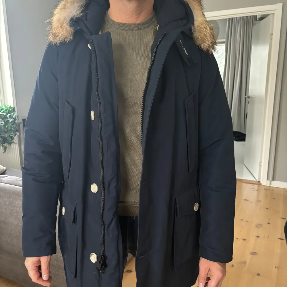 Säljer den klassiska Woolrich Arcric Parka i snygg mörkblå färg i storlek L som endast använts ca 5 ggr och är i nyskick. Jackan är inköpt på Länna Sport. Jackan har en avtagbar huva med pälsdetaljer och stängs med både dragkedja och knappar. Perfekt för kalla vinterdagar med sina stora fickor och varma foder. Passar både till vardags och lite finare tillfällen. 🧥❄️. Jackor.