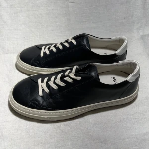 Svarta sneakers från Sweyd - Snygga svarta sneakers i skinn från Sweyd. De har vita snören och en vit sula som ger en stilren look. Perfekta för både vardag och fest! Skorna kommer med en praktisk tygpåse för förvaring. Ny pris är 2900 som ni kan se på sista bilden vårt pris 2600 pris kan diskuteras vid snabb affär storlek 42 men sitter som 43 🫡