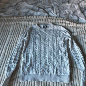 Grå kabelstickad tröja  - Säljer en stilren grå kabelstickad tröja . Perfekt för kyliga dagar med sin mjuka och bekväma passform. Tröjan har långa ärmar och en klassisk rund halsringning. Passar både till vardags och lite finare tillfällen. 🧶