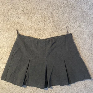 Grå minikjol från Zara - Säljer den perfekta gråa minikjolen från Zara i mycket bra skick. Kjolen har inbyggda shorts och veckade detaljer som ger en snygg och elegant look. Perfekt för både vardag och festliga tillfällen. Passar utmärkt till höst- och vårgarderoben!