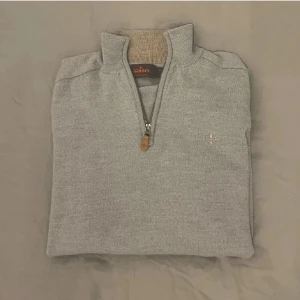 Grå merinoulltröja från Morris - Säljer en stilren grå tröja från Morris i 100% merinoull. Tröjan har en praktisk dragkedja framtill och en liten broderad detalj på bröstet. Perfekt för både höst och vinter, och den är i mycket bra skick. Supermjuk och varm! Passar bättre s då den krympt i tvätten!!