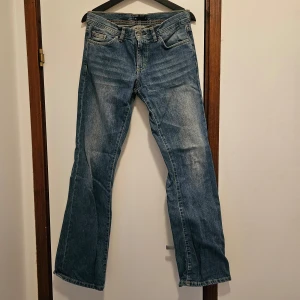 Blå bootcut jeans från attitude - Säljer ett par klassiska blå bootcut jeans från att. i storlek 29. De har en snygg tvätt med lätt slitna detaljer och fem fickor. Perfekta för en avslappnad stil och passar till alla tillfällen. Sköna och stilrena!