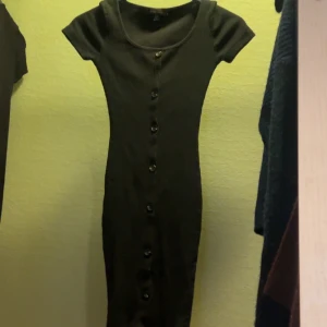 Svart klänning från Amisu - Snygg svart klänning från Amisu i storlek EU 32. Den är ribbad med knappar längs framsidan och har korta ärmar. Perfekt för både vardag och fest!