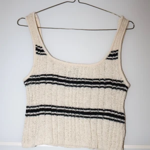 Beige stickad linnetopp med svarta ränder - Säljer en superfin beige stickad linnetopp med svarta ränder. Den är perfekt för både sommar och vår, och har en skön, ribbad textur. Toppen är ärmlös och har en avslappnad passform. Perfekt för en casual look eller att styla upp med accessoarer!