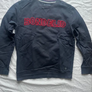 Svart tröja från Bondelid - Säljer en svart långärmad tröja från Bondelid i storlek M. Den har ett rött broderat Bondelid-tryck på framsidan. Perfekt för höst och vinter, och den är i bra skick. Skön och stilren för vardagsbruk!