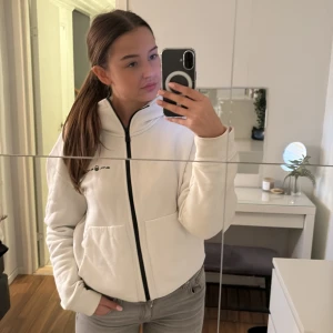 Vit sail racing hoodie med dragkedja - Säljer en supermjuk och varm vit sail racing hoodie med dragkedja framtill. Perfekt för kyliga dagar och har en stilren design. Hoodien har långa ärmar och två praktiska fickor. Passar både till vardags och för mysiga hemmakvällar.