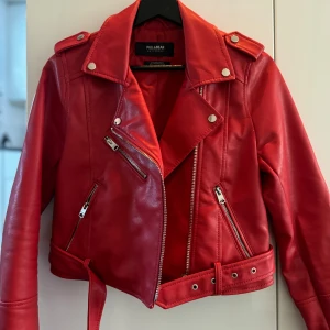 Röd skinnjacka från Pull&Bear - Säljer en snygg röd skinnjacka från Pull&Bear i mycket bra skick. Jackan har en cool bikerstil med dragkedjor och ett bälte i midjan. Perfekt för höst och vår, och den är långärmad. Passar perfekt för en fest eller en utekväll! Frakt ingår.