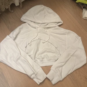 Vit croppad hoodie  - Säljer en superfin vit croppad hoodie från H&M Divided i storlek XS. Den är perfekt för en avslappnad stil och har en justerbar huva med dragsko. Materialet är en skön blandning av bomull och polyester. Perfekt för både vår och höst!