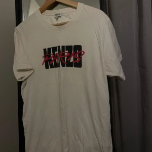 Vit Kenzo Paris T-shirt - Säljer en snygg vit Kenzo T-shirt med en stilren text i storlek L (passar även S/M), perfekt för vardagsbruk. T-shirten är i bra skick och gjord av mjukt material. Passar perfekt till jeans eller shorts.