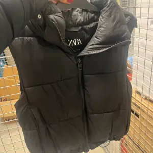 Säljer en svart dunväst från Zara i mycket bra skick. Västen har en dragkedja framtill och är perfekt för kyligare väder. Den är stilren och passar till många olika outfits. Perfekt för höst och vår! Man kan även dra åt den längst ner så den blir tightare 