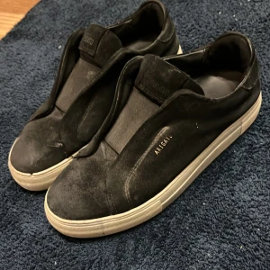 Svarta sneakers från Axel Arigato - Säljer ett par svarta sneakers från Axel Arigato i bra skick. De har en stilren design med vit sula och är perfekta för vardagsbruk. Skorna är gjorda av mocka  och har en diskret logga på sidan. Passar bra till både jeans och mer uppklädda outfits. Ny pris 2650kr köpta på NK fick i jullklapp mitt pris 1300 