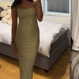 Guldglittrig långklänning - Säljer en fantastisk guldglittrig långklänning som är perfekt för festliga tillfällen. Klänningen har en tight passform och är axelbandslös, vilket ger en elegant look. Materialet är glittrigt och fångar ljuset vackert. Perfekt för nyår eller andra speciella tillfällen! ✨ Klänningen är genomskinlig, jag har en underklänning under