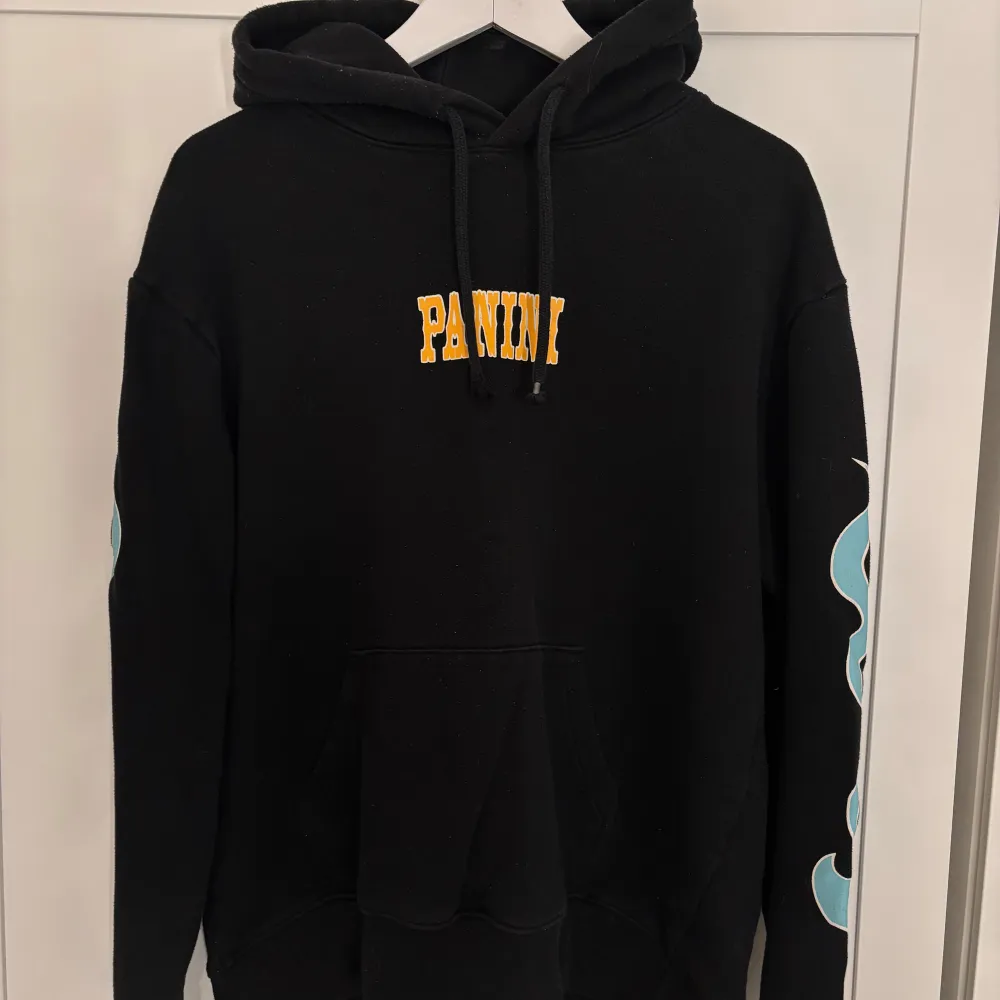 Cool svart hoodie från H&M Divided med blåa flammor längs ärmarna och texten 'LIL NAS X' på ryggen. Framsidan har texten 'PANINI' i gult. . Tröjor & Koftor.