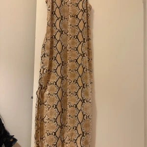 Ormmönstrad långklänning - Säljer en supercool ormmönstrad långklänning med smala axelband. Perfekt för en utekväll eller en sommarfest. Klänningen har en avslappnad passform och är gjord i ett lätt material som känns skönt mot huden. Ett måste för garderoben om du älskar djurmönster!