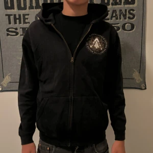 Svart hoodie med tryck - Säljer en svart hoodie med coolt tryck både fram och bak. Den har en dragkedja och är perfekt för höst och vinter. Storleken är normal och den är i bra skick. Grym för både vardag och chill.