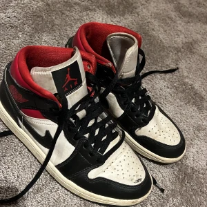 Nike Air Jordans i svart, vitt och rött - Säljer ett par klassiska Nike Air Jordans i svart, vitt och rött. Skorna har snörning och den ikoniska Air Jordan-loggan på sidan. De är i bra skick med lite slitage på sulorna. Perfekta för både vardag och sportiga tillfällen!