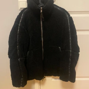 Ny teddyjacka pilejacka i stl M från HM - Ny med tags. Svart i storlek M  En svart tjock och varm teddyjacka i mjuk pile med kantband i ytbehandlad kvalitet. Jackan har lös passform, ståkrage, tvåvägsdragkedja fram och kängurufickor. Fodrad. Oversize. 