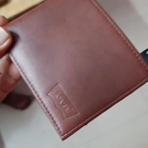 Brun plånbok från Levi's - Säljer en snygg brun plånbok från Levi's i skinn. Den har flera fack för kort och sedlar, perfekt för att hålla ordning på dina grejer. Plånboken är i nyskick och har en stilren design med Levi's-loggan präglad på framsidan. Perfekt accessoar för vardagsbruk!