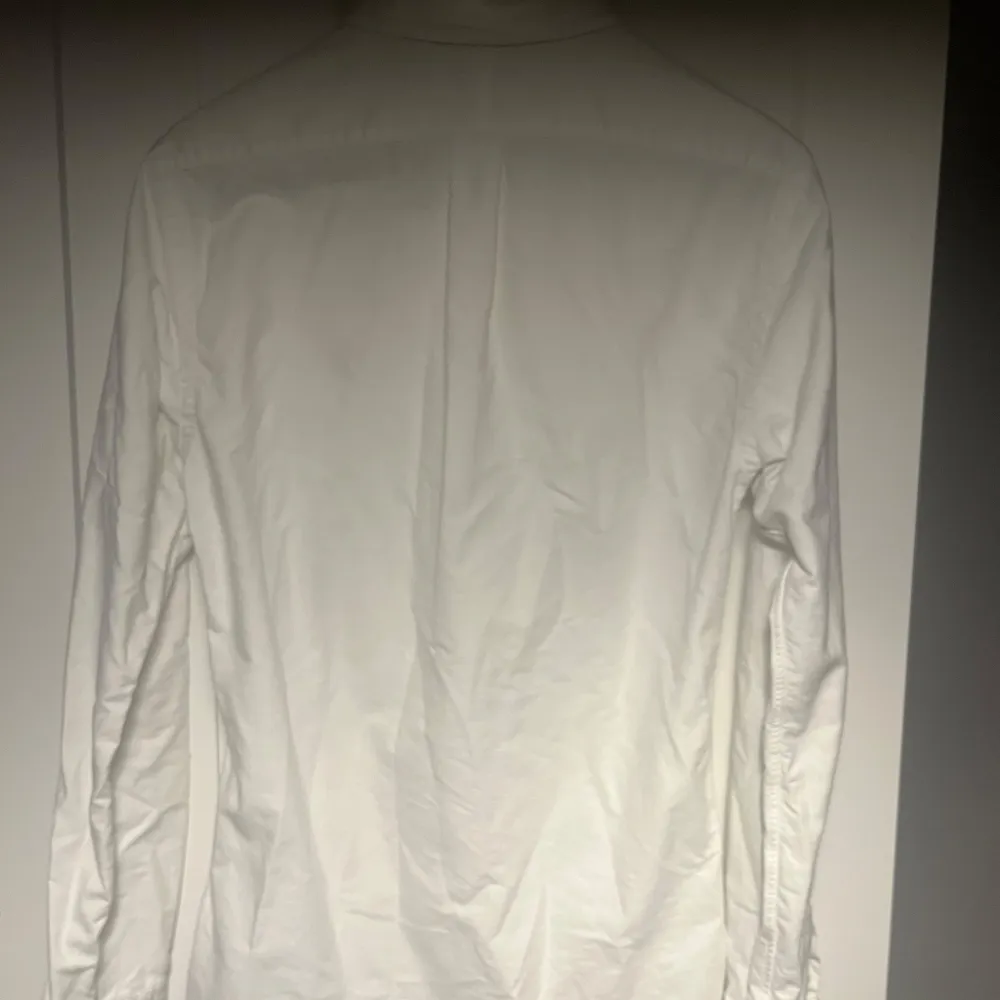 Säljer en stilren vit skjorta från Ralph Lauren i slim fit. Skjortan har långa ärmar och klassiska knappar framtill. Perfekt för både vardag och festliga tillfällen. Den är i bra skick och redo för en ny ägare!. Skjortor.