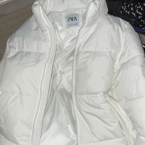 Vit pufferjacka från Zara - Säljer en superfin vit pufferjacka från Zara i storlek S. Jackan är perfekt för kalla dagar med sin mysiga och varma design. Den har en dragkedja framtill och är i mycket bra skick. Perfekt för både höst och vinter! 