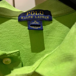 Grön pikétröja från Ralph Lauren - Säljer en snygg grön pikétröja från Ralph Lauren i storlek XL (barn) skulle säga att den är som en M/S. Tröjan har en klassisk krage med knappar och det ikoniska Ralph Lauren-loggan broderad på bröstet. Perfekt för både vardag och fest! 💚