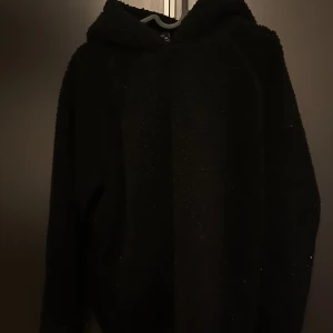 Svart teddyjacka från Urban Classics - Mysig svart teddyjacka från Urban Classics i storlek M. Perfekt för kyliga dagar med sin fluffiga och varma design. Jackan har långa ärmar och en bekväm passform. Ett måste för höst- och vintergarderoben!