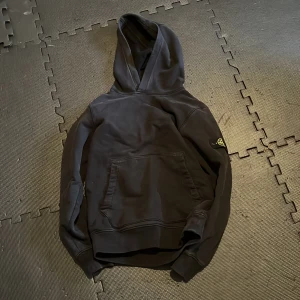 Svart hoodie från Stone Island - Säljer en svart hoodie från Stone Island i bra skick. Den har en klassisk känguruficka och en snygg logga på ärmen. Perfekt för höst och vinter, och den är superbekväm att ha på sig. Passar både till vardags och chillkvällar. 🖤