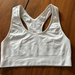 Vit sporttopp från Panos Emporio - Säljer en vit sporttopp från Panos Emporio i storlek M. Den är tillverkad av 98% nylon och 2% polyester med quick-dry funktion, perfekt för träning. Toppen har en racerback-design för extra stöd och komfort. Aldrig använd. Djur och rökfritt hem.