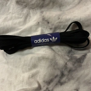 Svarta skosnören från Adidas - Säljer ett par klassiska svarta skosnören från Adidas. Perfekta för att ge dina sneakers en ny look eller ersätta gamla snören. Passar de flesta skotyper och ger en stilren touch. Helt nya och oanvända!