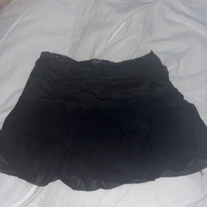 Svart kjol med spetsdetaljer - Snygg svart kortkjol med spetsdetaljer upptill. Perfekt för en utekväll eller fest! Kjolen har en elegant och feminin stil som passar till många olika tillfällen. Den har ett stretch material så passar xs-s