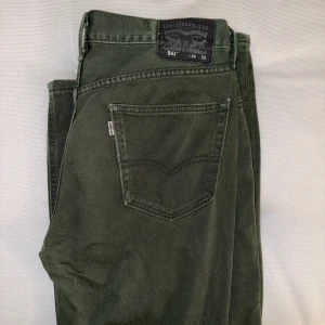 Gröna Levis 541 34x32 - Gröna Levis köpta second hand. Sällsynt färg! Mindre hål i vänster ben. Sitter fint i midjan med bälte på mig som vanligtvis har 32x32, 189cm. 