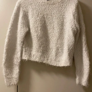 Vit fluffig tröja - Mysig vit tröja i fluffigt material, perfekt för kyliga dagar. Den har en croppad passform och långa ärmar, vilket gör den både trendig och bekväm. Perfekt att matcha med jeans eller kjol för en avslappnad look.
