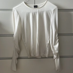 Gina tricot blus - Gina tricot blus i vit. Räfflade ärmar med en slits längst ner. Lite missfärgning i linningen.