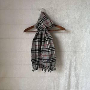 Burberry halsduk - Säljer en klassisk grå halsduk från Burberry. Den är i 100% lammull. Perfekt för att hålla sig varm under höst och vinter. Den har ett tidlöst mönster med inslag av rött och svart. Superfin att ha både till vardags och fest!passar för både vinter som höst.          Skicket är 9/10 utan defekter och äkta såklart👍 vid frågor är det bara att höra av sig👍