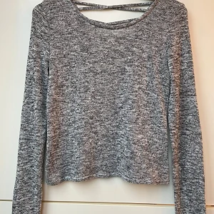 Grå stickad tröja från H&M Divided - Säljer en grå stickad tröja från H&M Divided med snygg snörning i ryggen. Tröjan har långa ärmar och en rund halsringning fram. Perfekt för en stilren och bekväm look.