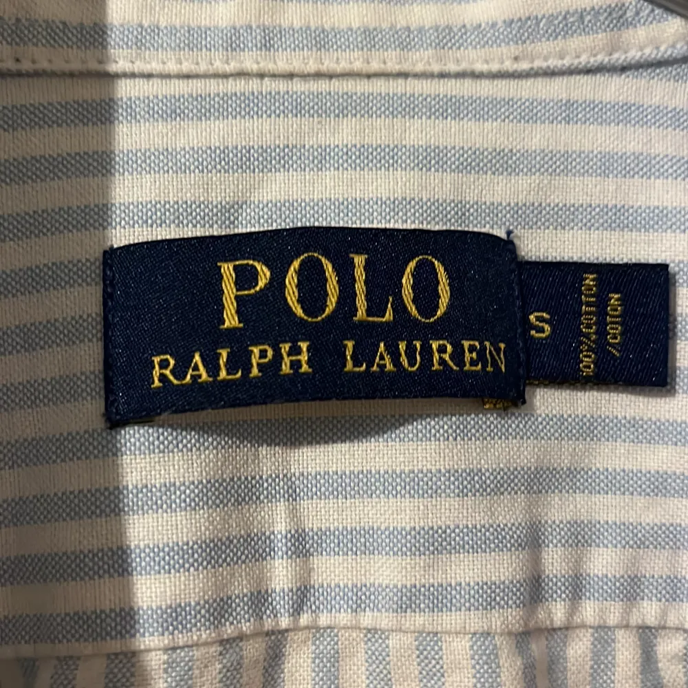Snygg och klassisk ljusblå och vit randig skjorta från Polo Ralph Lauren. Skjortan har långa ärmar och en broderad logotyp på bröstet. Perfekt för en stilren look. . Paidat.