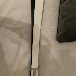 Vit och svart bälte med silverdetaljer - Snyggt bälte i vitt och svart med en stilren silverfärgad spänne. Perfekt för att ge en elegant touch till din outfit. Bältet har en klassisk design och flera hål för justerbar passform.