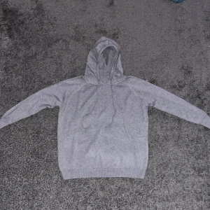 Grå merinoull hoodie - Säljer en stilren grå hoodie med dragsko i huvan. Perfekt för en avslappnad look. Den har långa ärmar och ribbade muddar vid ärmslut och nederkant. Merinoull. Helt ny, pris kan diskuteras vid snabb affär. Slim fit